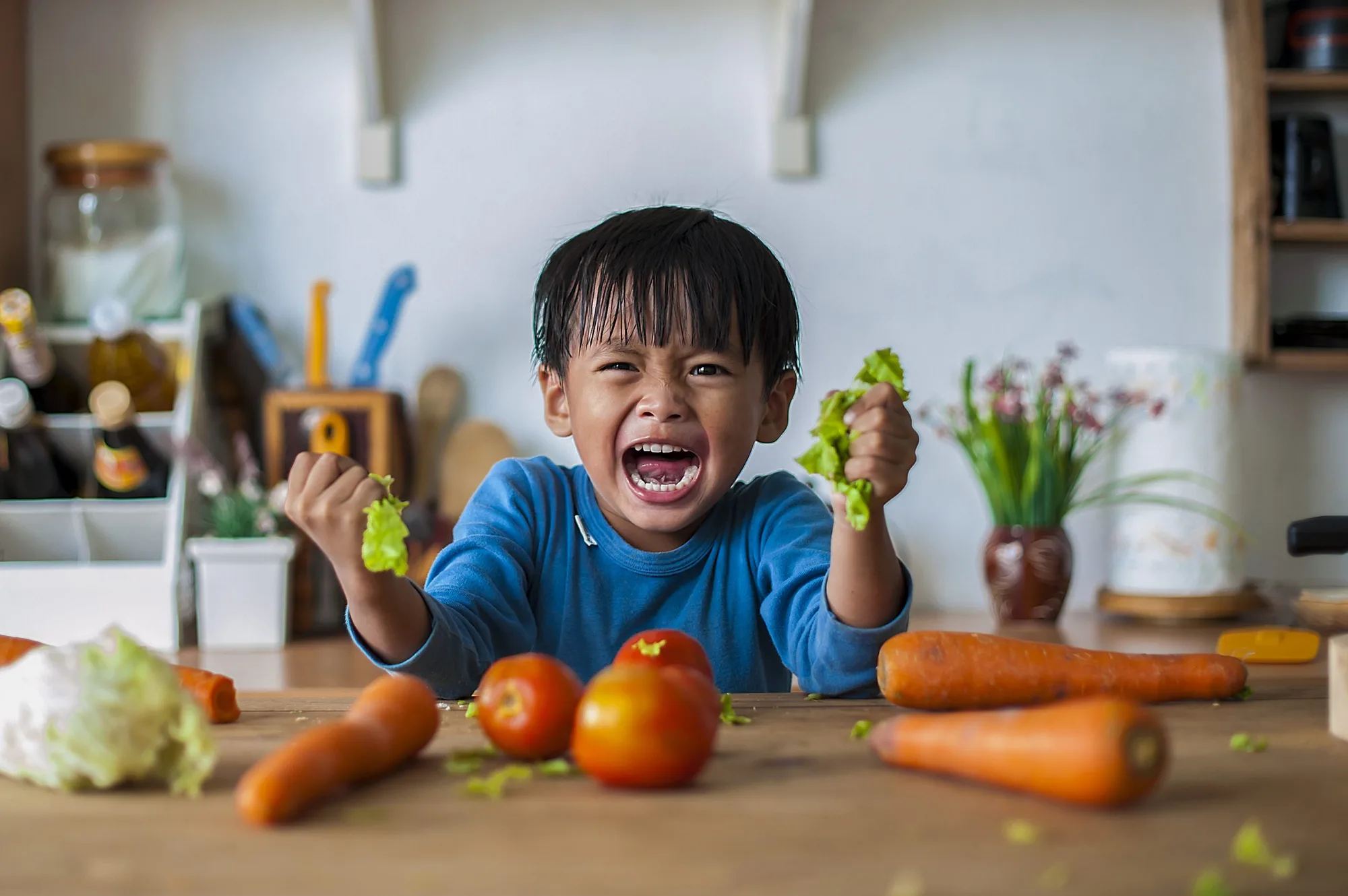 Upset boy at a kitchen table with vegetables